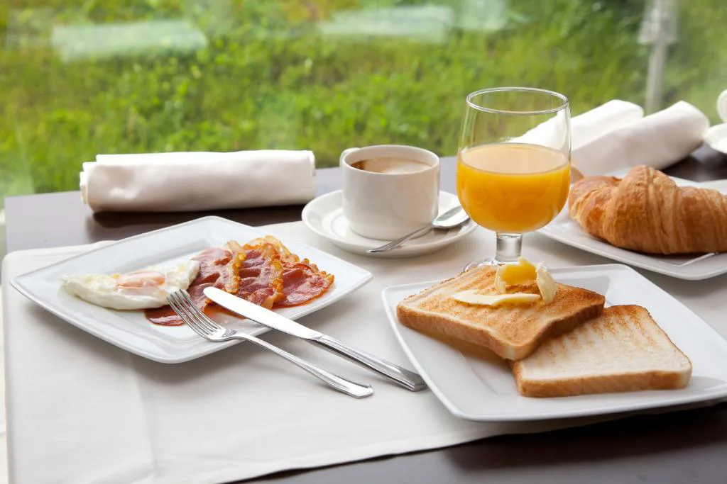 Desayuno servido con café, zumo y croissant junto a la ventana, Hotel Las Sirenas