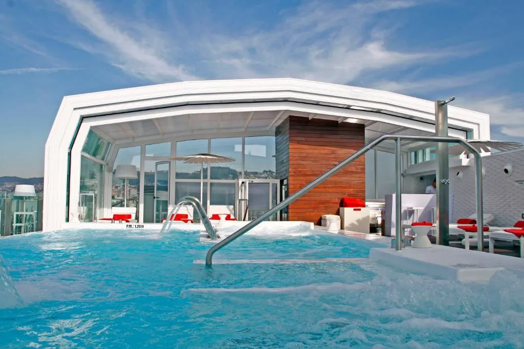 Piscina exterior climatizada en la azotea del hotel con tumbonas rojas