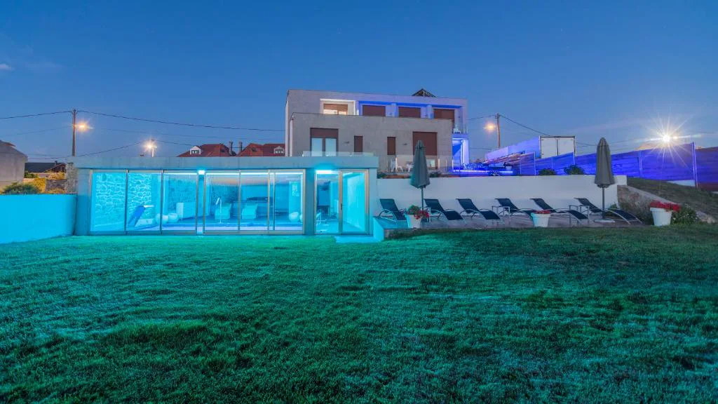 Spa iluminado en azul visto desde el jardín al atardecer, con la casa al fondo, Hotel Naturaleza Mar da Ardora