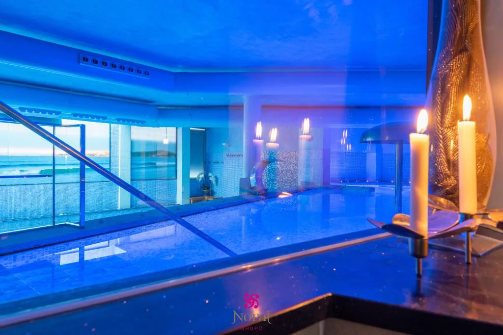 Piscina de hidroterapia con velas encendidas y vistas al mar a través del ventanal, Hotel Norat Marina & Spa