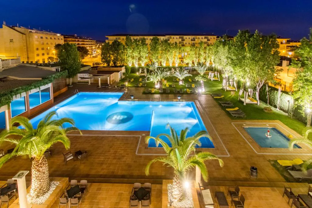Piscina iluminada al anochecer entre jardines y palmeras