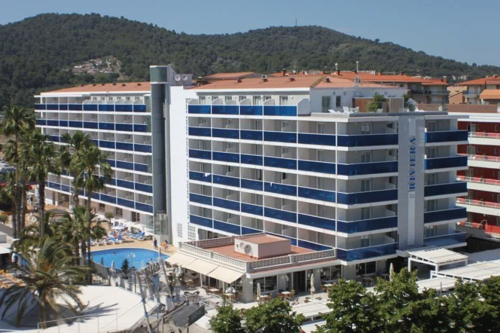 Hotel de fachada azul con piscina y palmeras en primer plano