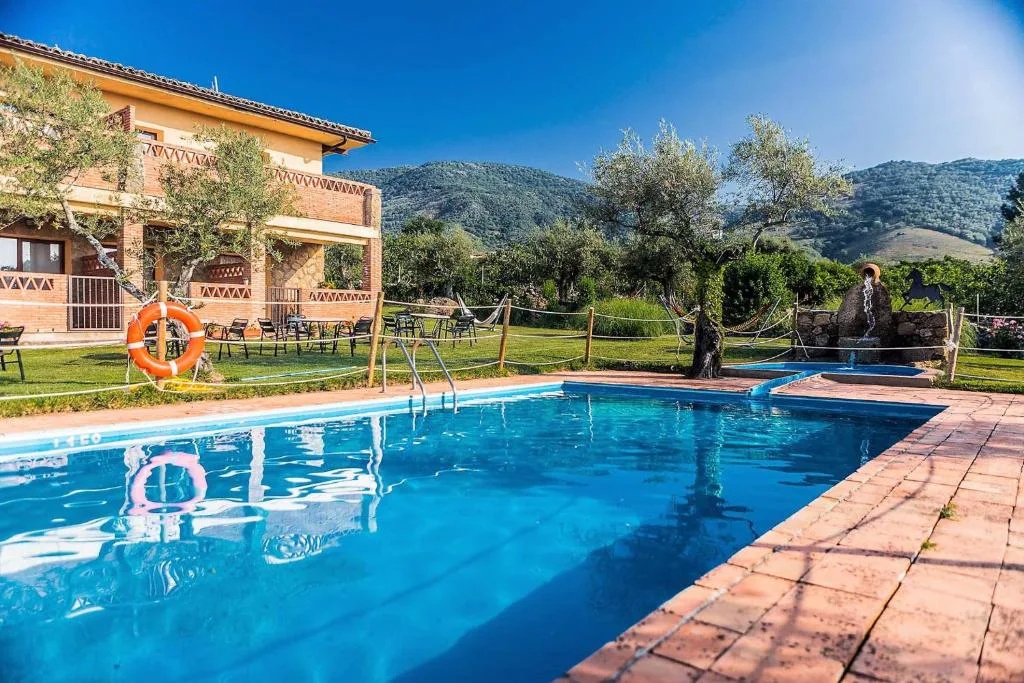 Piscina rodeada de jardín y sombrillas con montañas al fondo