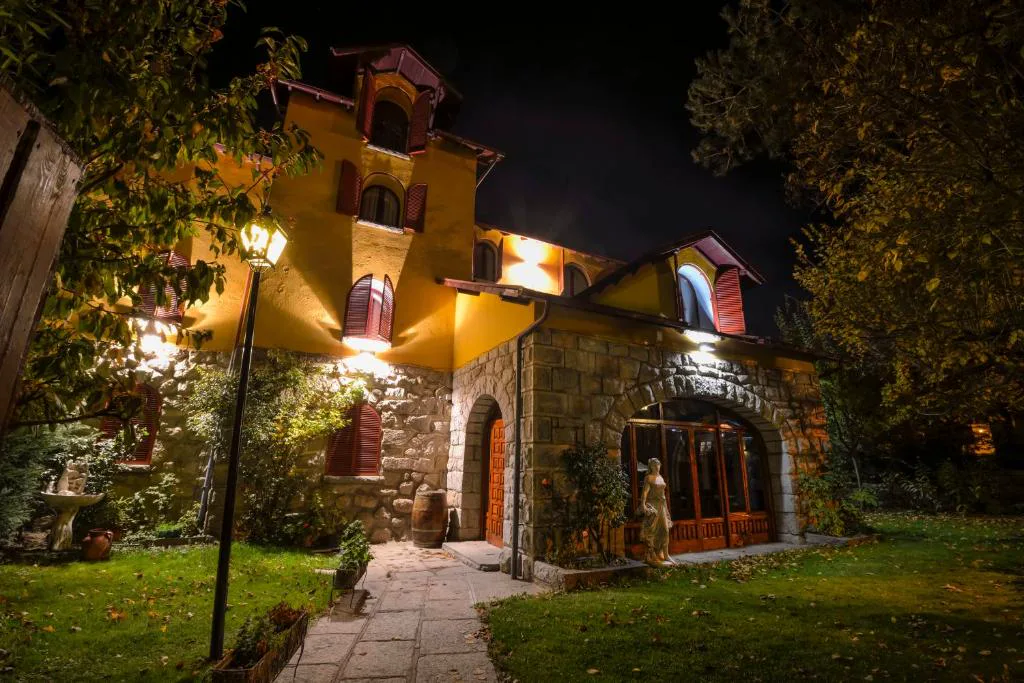 Hotel de piedra iluminado de noche entre jardín y farolas