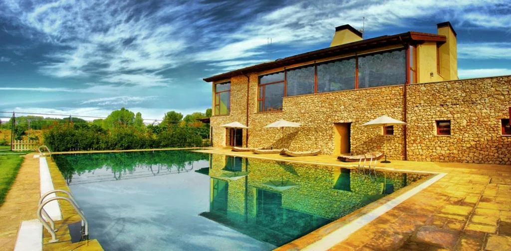Edificio de piedra con piscina al atardecer y jardín
