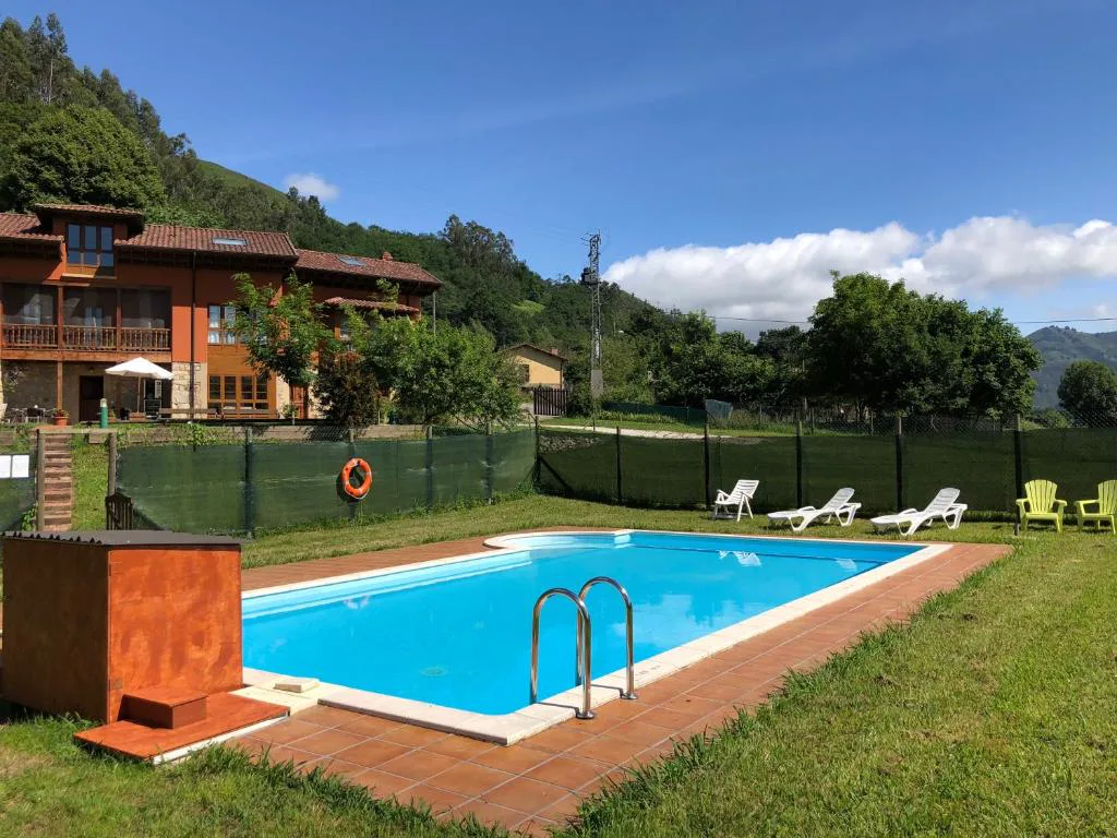 Piscina rectangular con tumbonas y casas de madera al fondo