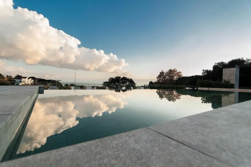 Borde de una piscina que refleja las nubes y el cielo