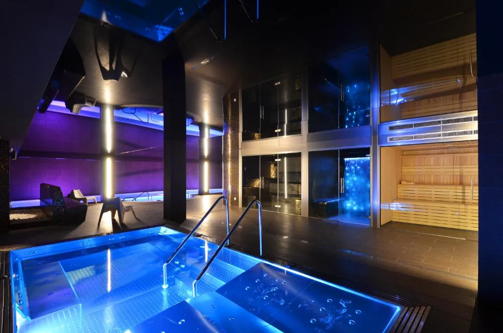 Piscina de spa iluminada en azul junto a una sala de madera