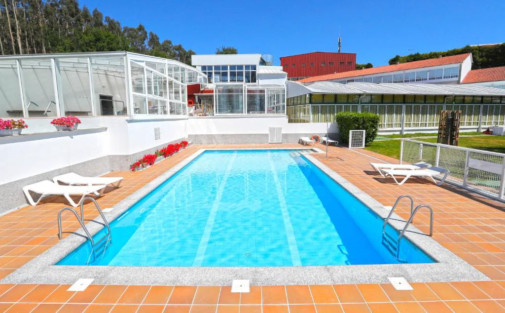 Piscina exterior con escalerillas de acceso junto a tumbonas blancas, Hotel Spa Congreso