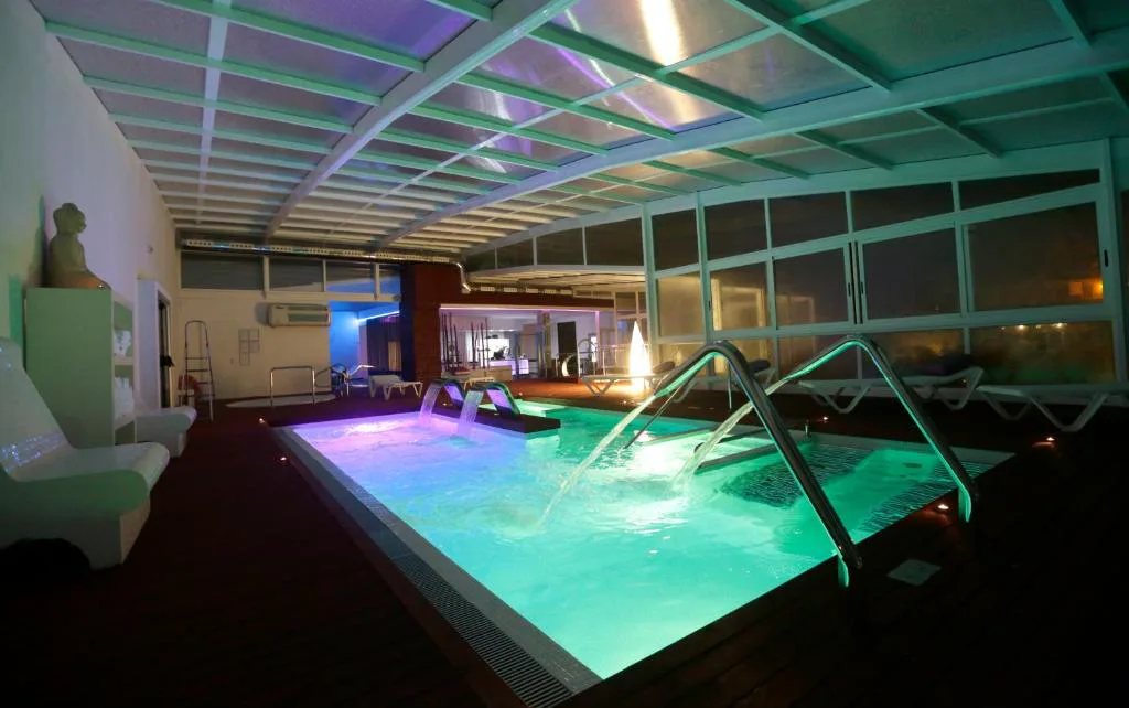 Piscina de hidroterapia interior con chorros de colores bajo techo acristalado por la noche, Hotel Spa Congreso, Teo