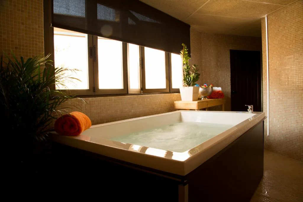 Bañera de hidromasaje con toallas enrolladas junto a una ventana con plantas, Hotel & Spa Entre Pinos
