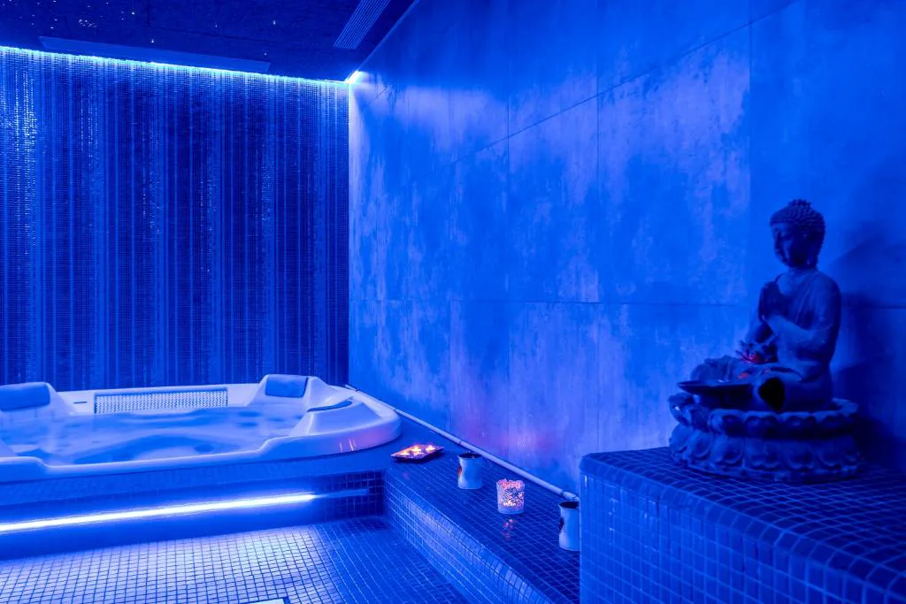 Sala de spa con jacuzzi iluminado en azul y estatua de Buda