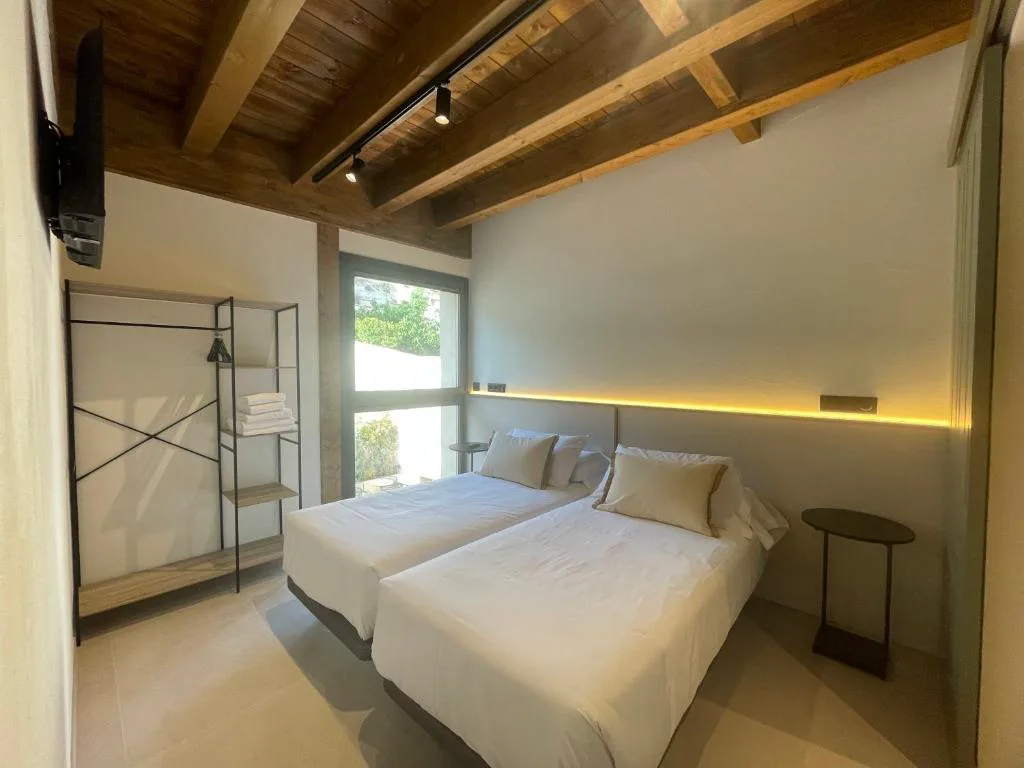 Habitación con vigas de madera, cama gemela y luz indirecta
