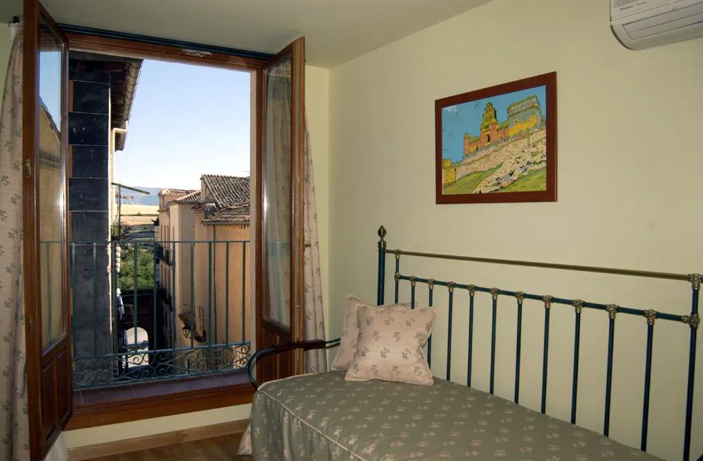 Habitación con cama de forja y ventana con vistas a los tejados