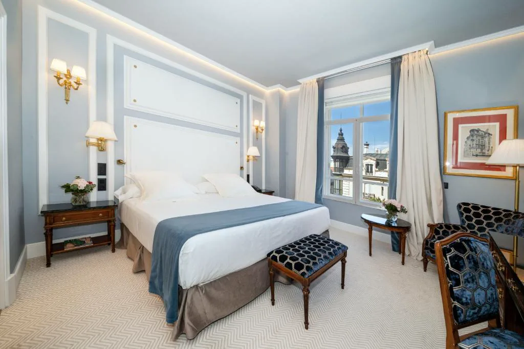Habitación con cabecero blanco, ropa de cama azul y vistas a un campanario