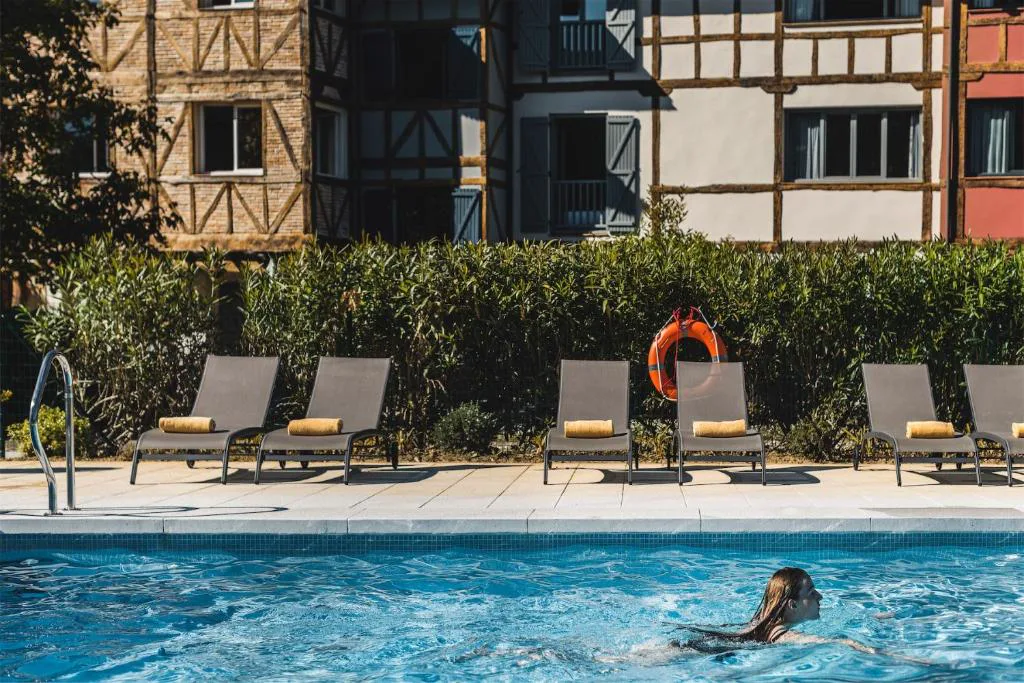 Nadador en la piscina con tumbonas y el hotel al fondo