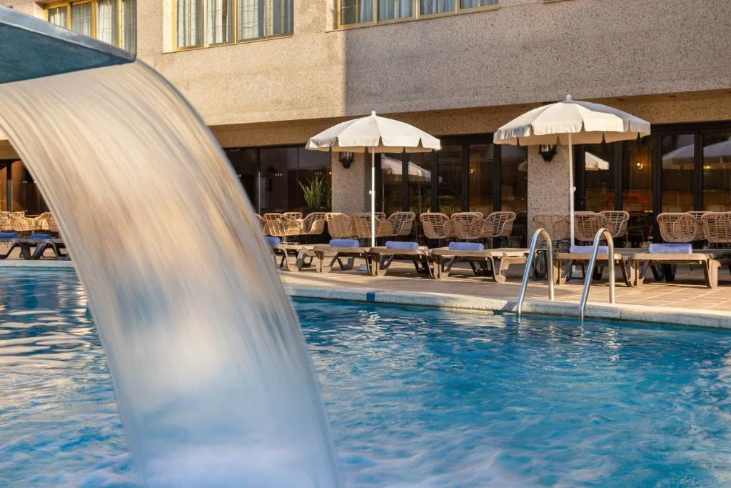 Piscina con cascada de agua y sombrillas junto al hotel