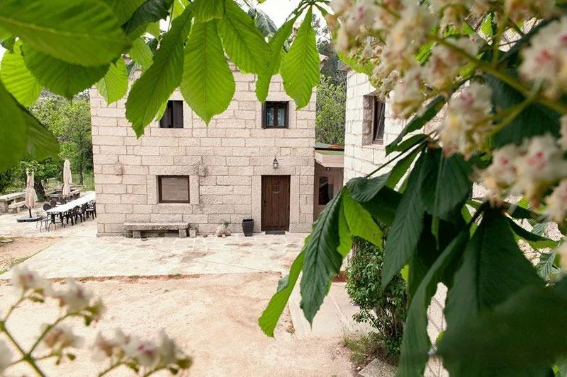 Casa de piedra entre árboles y flores al pie del convento