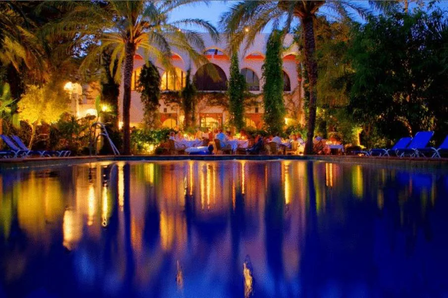 Piscina iluminada de noche frente a un edificio de estilo morisco