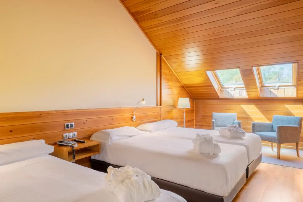 Habitación abuhardillada con dos camas y sillones junto a ventanas de tejado, IBERIK Augas Santas