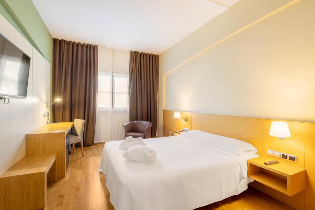 Dormitorio doble moderno con sillón de cuero y cortinas oscuras, IBERIK Augas Santas