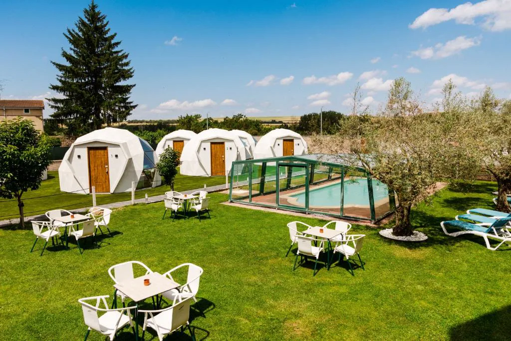 Igloos blancos sobre un jardín de césped con mesas blancas y una piscina cubierta al fondo