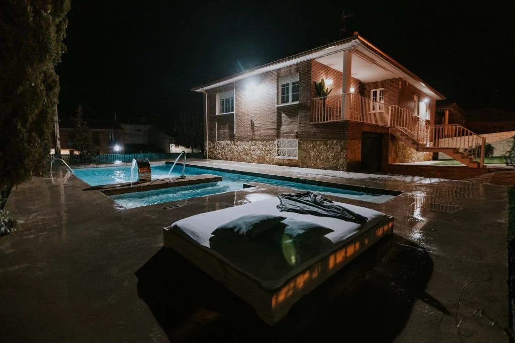 Piscina iluminada de noche junto a la casa