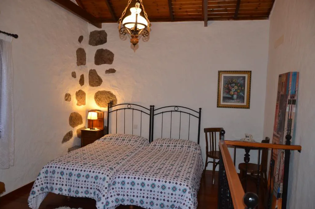Dormitorio con pared de piedra volcánica vista y camas de forja, La Berrera
