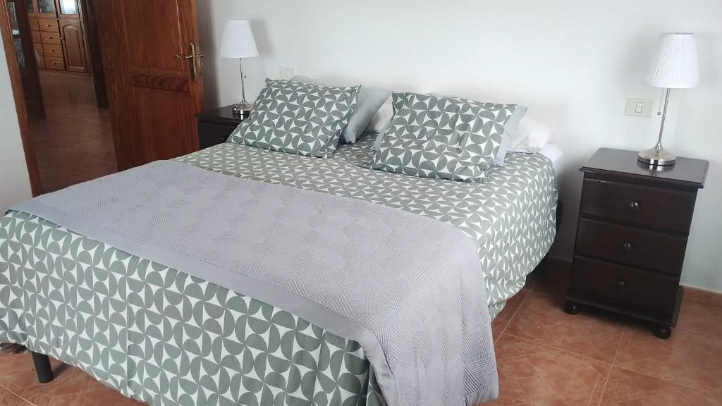 Dormitorio de matrimonio con ropa de cama gris y mesitas de madera oscura, La Caldereta Casa Rural