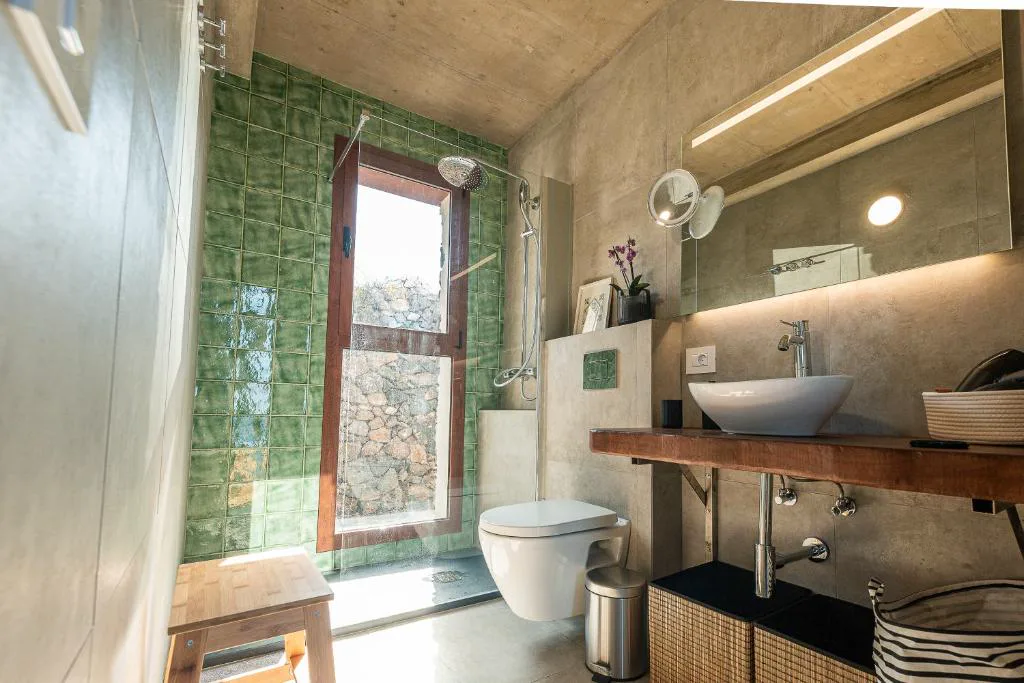 Baño con azulejos verdes y ventana con vistas a las piedras volcánicas, La Candia y el Mar