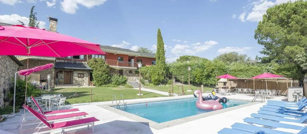 Piscina rodeada de sombrillas rosas y tumbonas con la casa al fondo