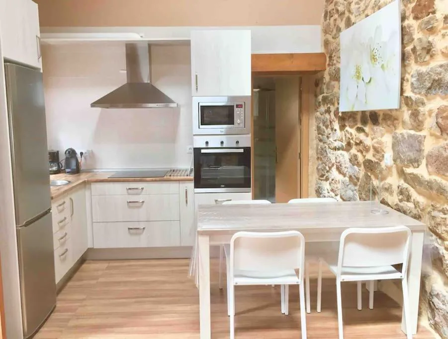 Cocina blanca con mesa y pared de piedra