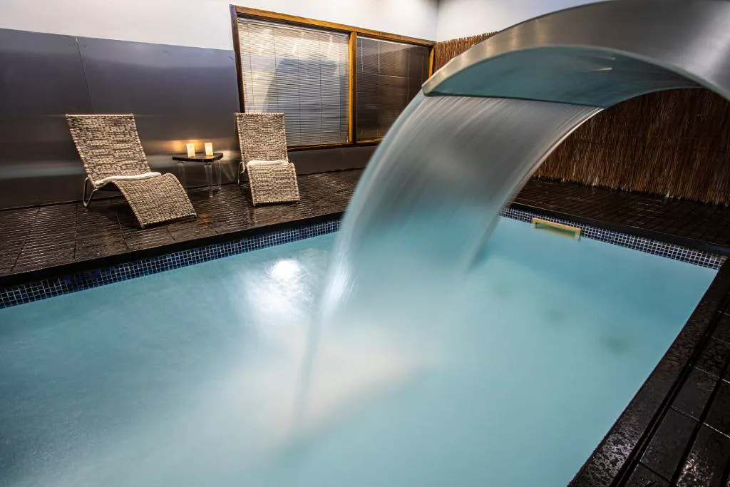 Piscina interior del spa con una cascada de agua y dos tumbonas de mimbre