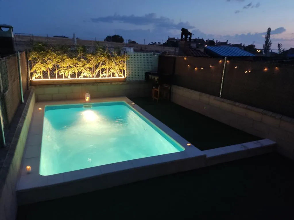 Piscina iluminada de noche con jardineras y luz cálida