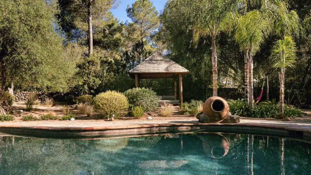 Zona chill out junto a la piscina con cabaña de madera y jarrón de barro tradicional, La Finca Agroturismo Can Bet