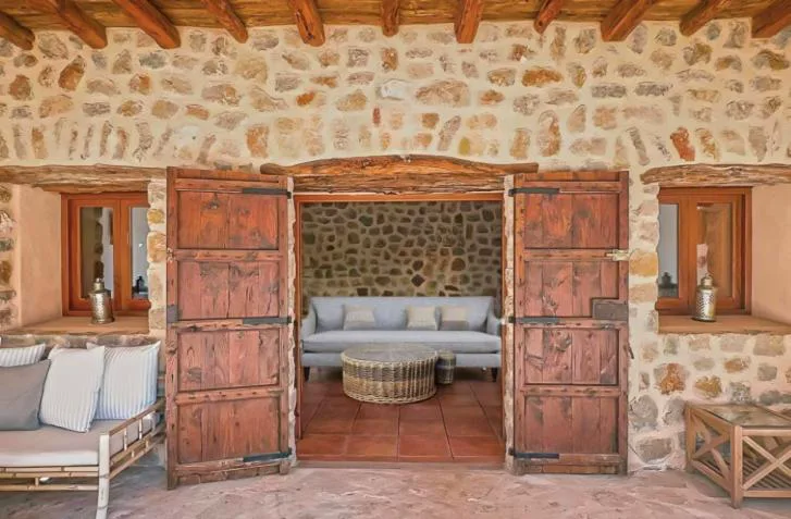 Salón de piedra vista con sofá gris y puertas de madera antiguas, La Finca Agroturismo Can Bet
