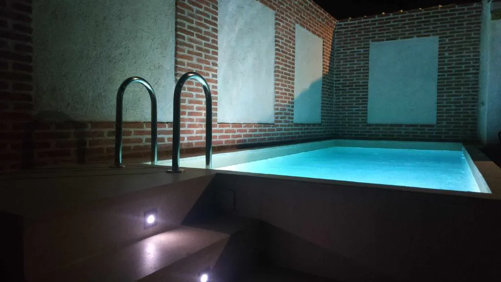Piscina iluminada por la noche entre muros de ladrillo