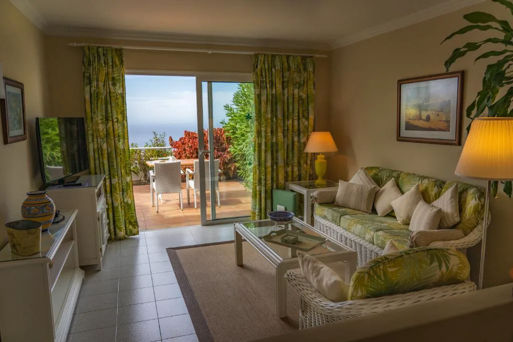 Salón con sofás de mimbre y vistas al jardín exterior, La Palma Jardín Resort