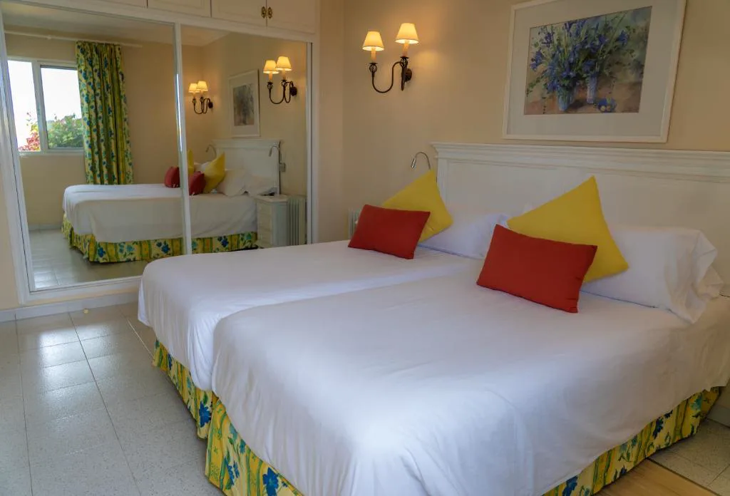 Dormitorio con colcha amarilla y floral, cuadro de flores en la pared, La Palma Jardín Resort