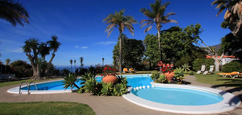 Bungaló blanco de tejado rojo entre palmeras y montañas de La Palma Jardín Resort, en El Paso
