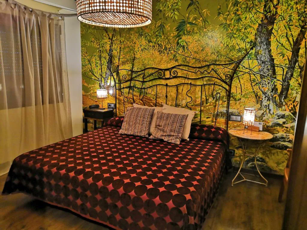 Habitación con cama de sábanas rojas y bosque en la pared