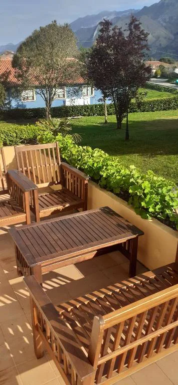 Terraza con mesa y sillas de madera sobre césped, con árboles al fondo