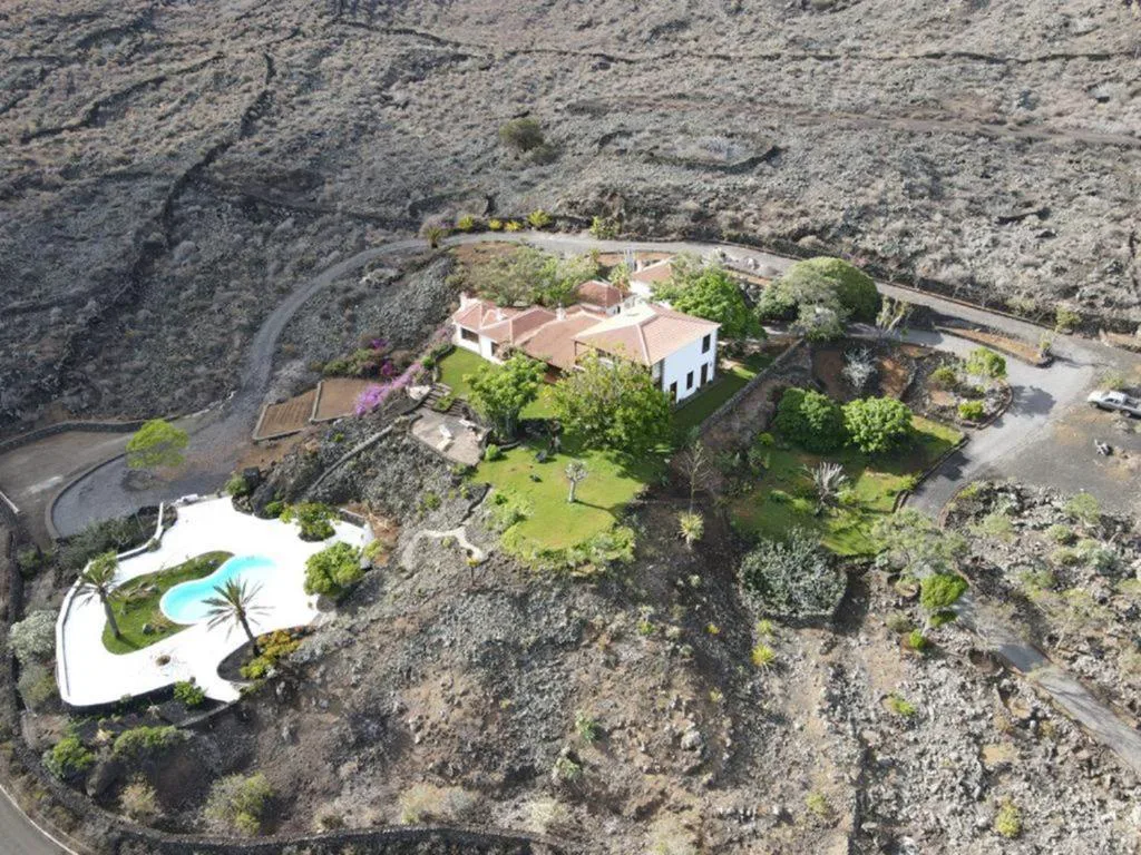 Vista aérea de la finca señorial con piscina, jardines y aparcamiento entre el paisaje volcánico, La Rayuela Suites Boutique