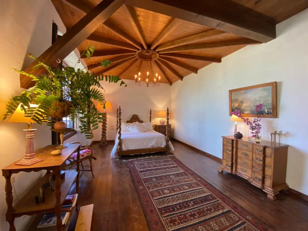 Dormitorio con cama de dosel de madera tallada bajo un techo radial de vigas y araña de cristal, La Rayuela Suites Boutique