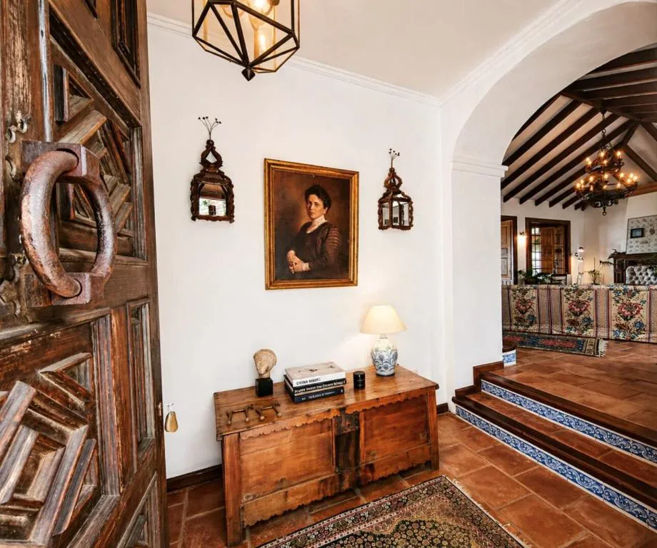 Recibidor con retrato antiguo, arcón de madera y arco de piedra hacia el salón, La Rayuela Suites Boutique
