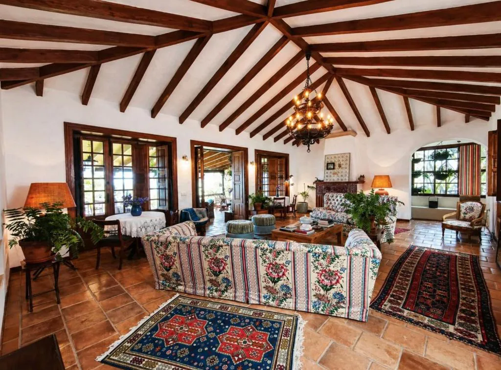 Salón con sofás de estampado floral, chimenea de piedra y vigas de madera vista, La Rayuela Suites Boutique