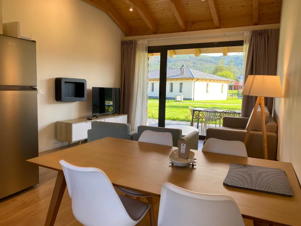 Salón comedor con mesa de madera, sillas blancas y vistas al jardín