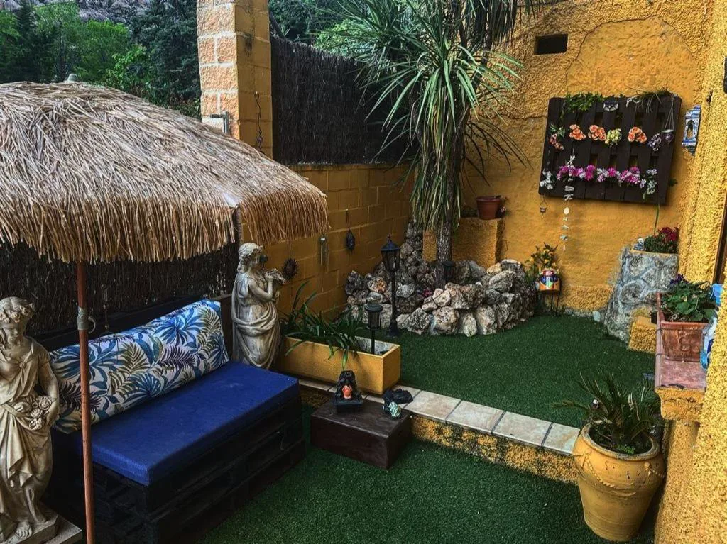 Rincón de jardín con sombrilla de paja, cojines azules y plantas