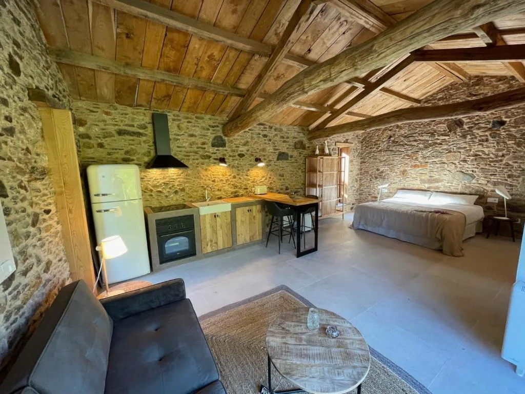 Estudio abierto con cocina, cama y paredes de piedra bajo techo de vigas, Lar do Gado