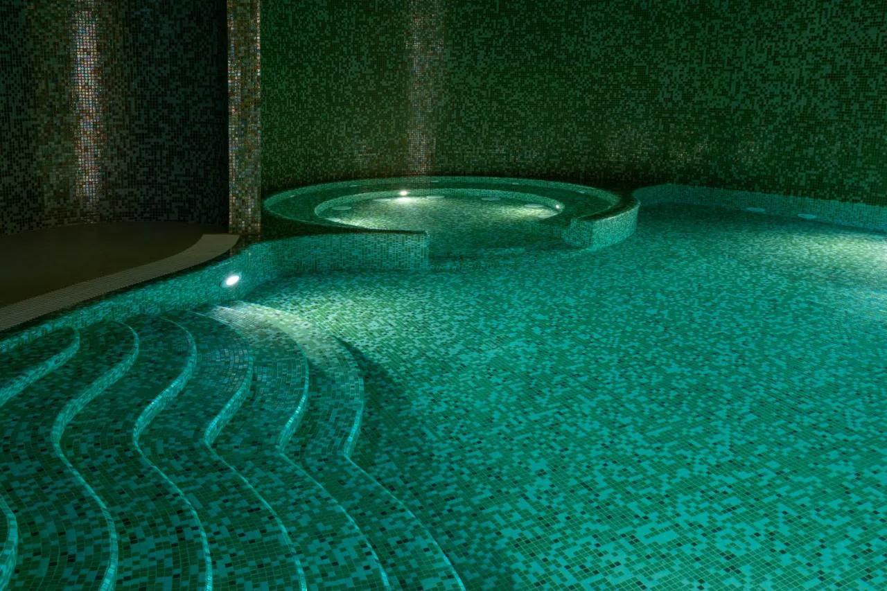 Piscina cubierta con mosaico verde y jacuzzi de Legacy Ithos Boutique Hotel